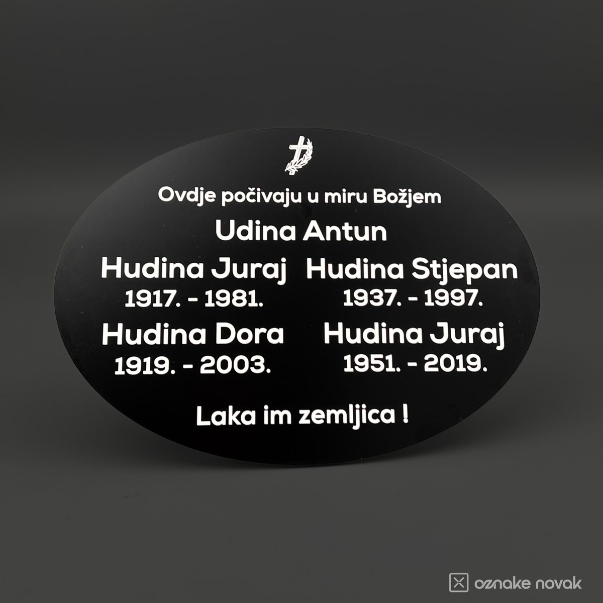 Black oval memorial plate with white engraved family names, dates and dedication