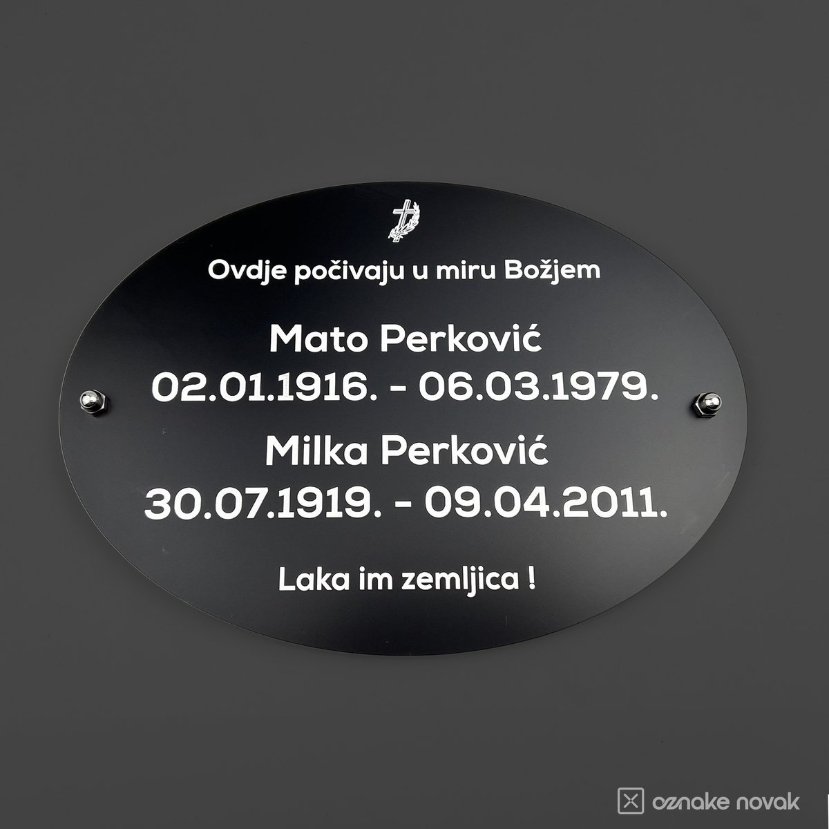 Black oval memorial plate with engraved names and full dates, mounted with screws