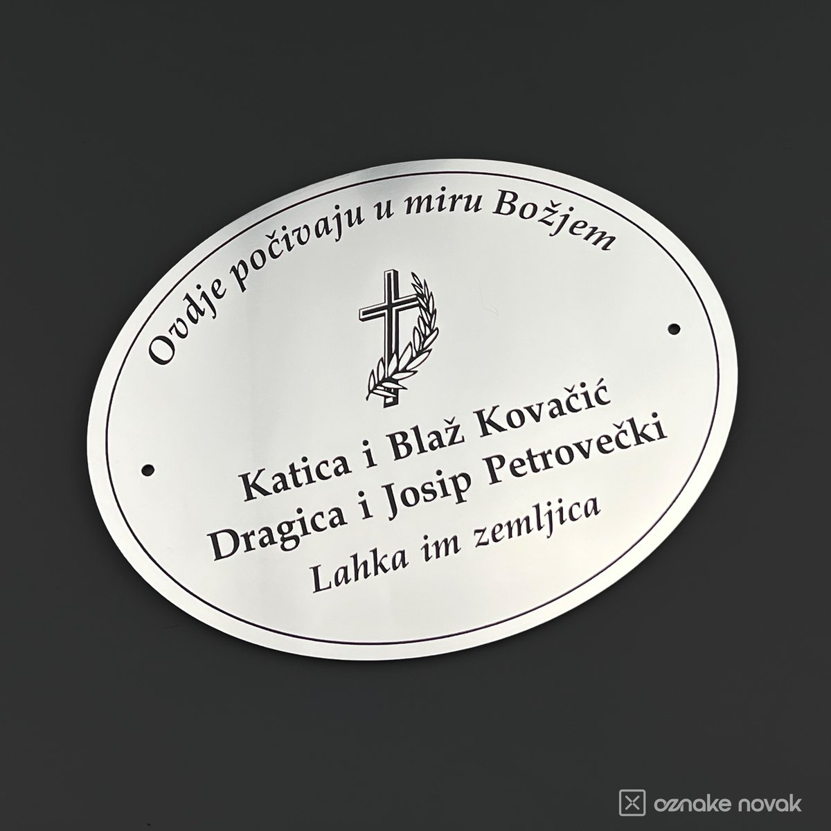 White oval memorial plate with black engraved names, a cross and arched dedication text