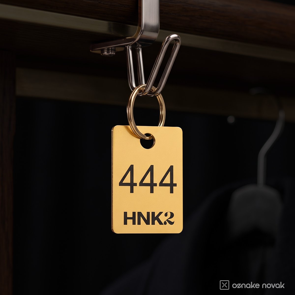 Brushed gold cloakroom tag number 444 with HNK2 logo hanging on a cloakroom hook