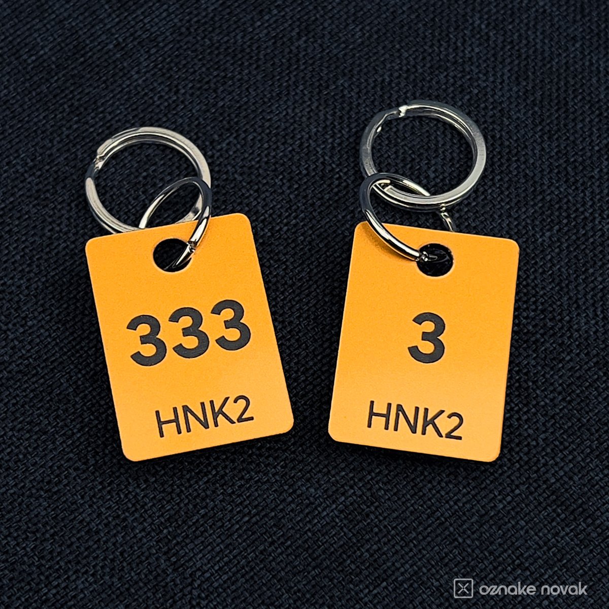 Smooth Gold cloakroom tag samples numbered 333 and 3 on dark fabric