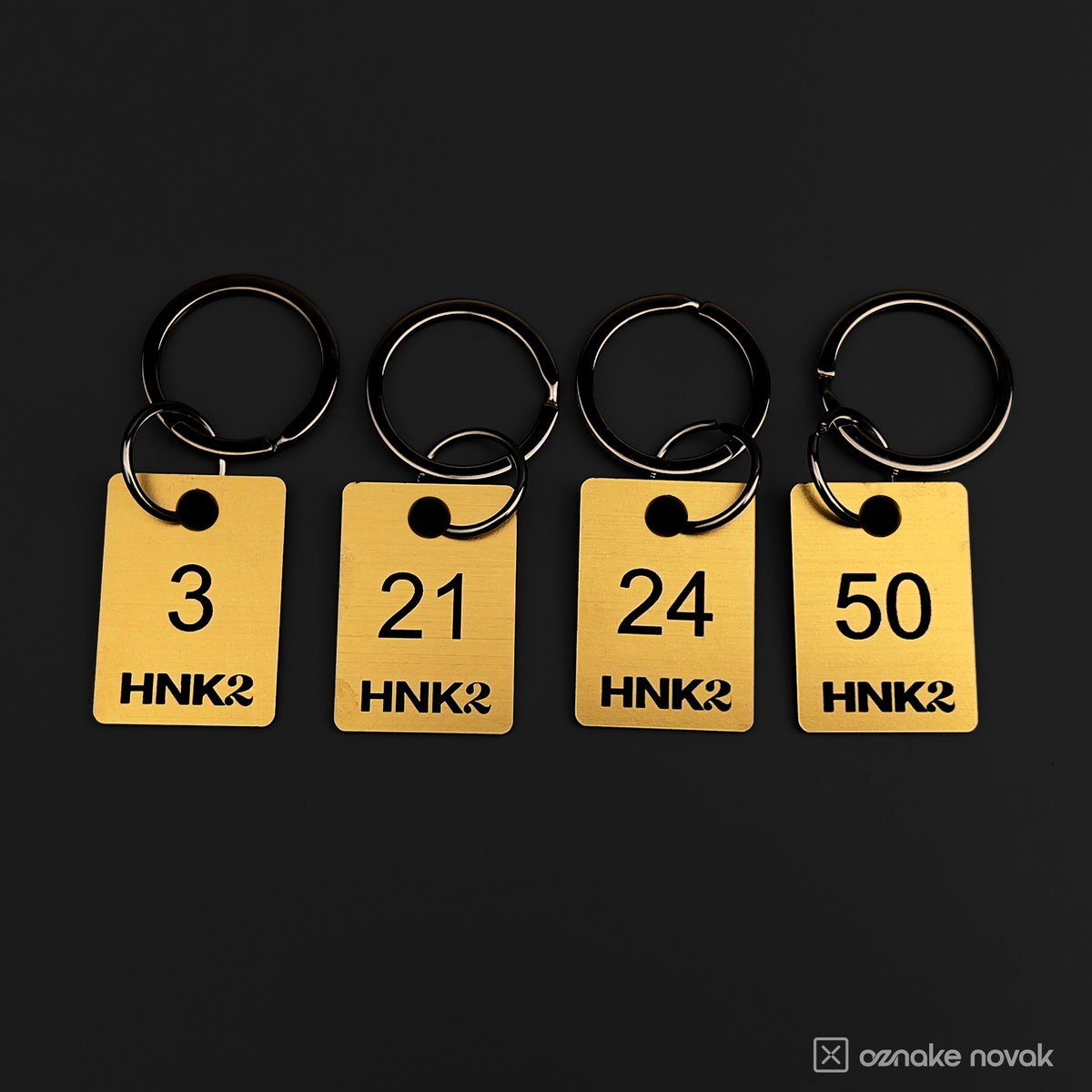 Four gold cloakroom tags numbered 3, 21, 24 and 50 with HNK2 logo