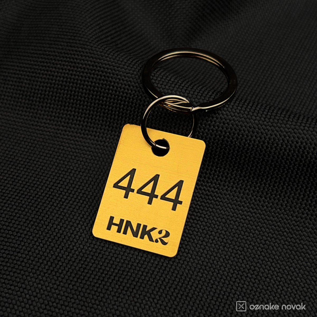 Close-up of a gold cloakroom tag number 444 with HNK2 logo and metal ring