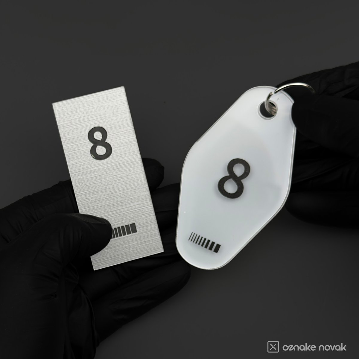 Gloved hands holding a brushed metal name plate and an opal white key tag, both numbered 8