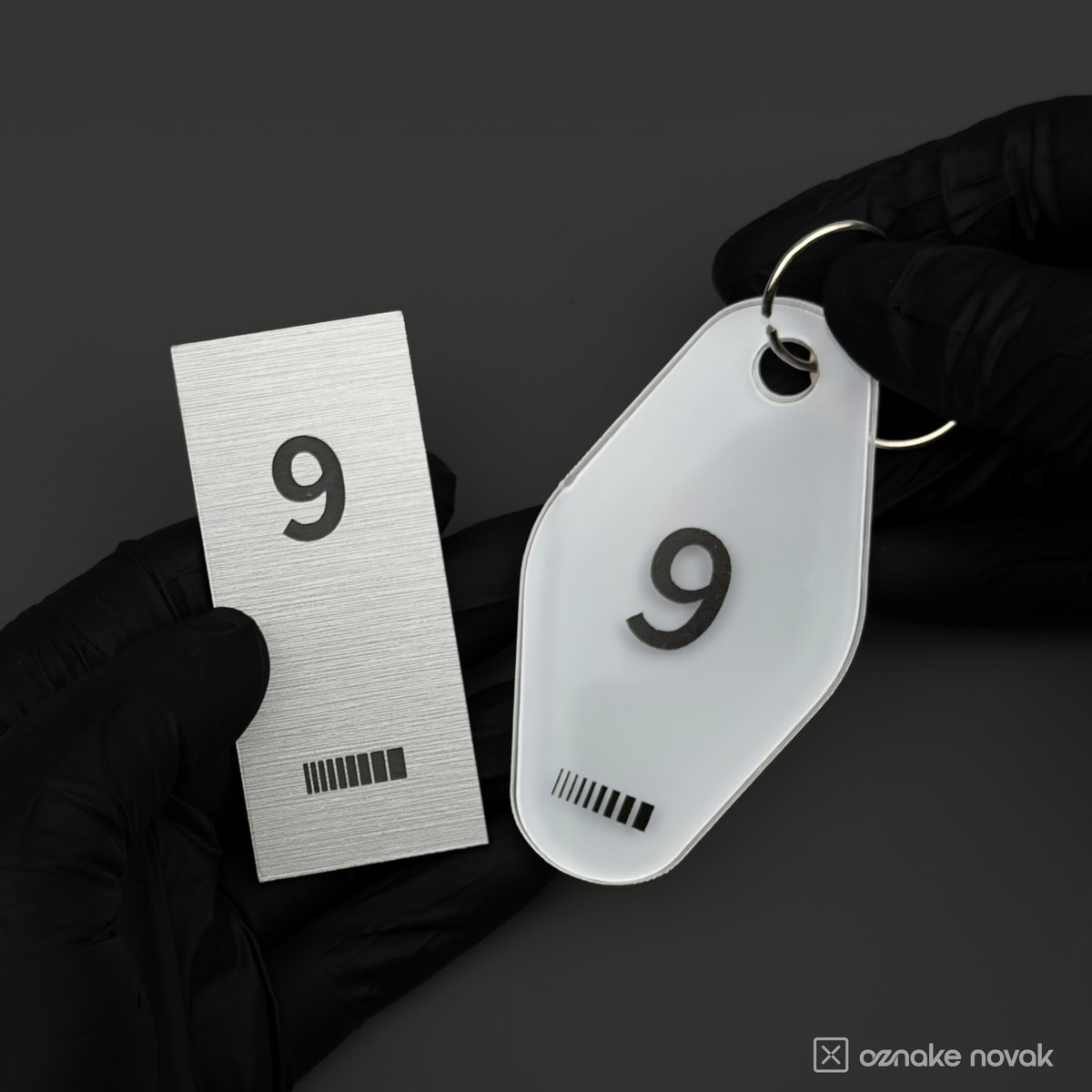 Gloved hands holding a brushed metal name plate and an opal white key tag, both numbered 9