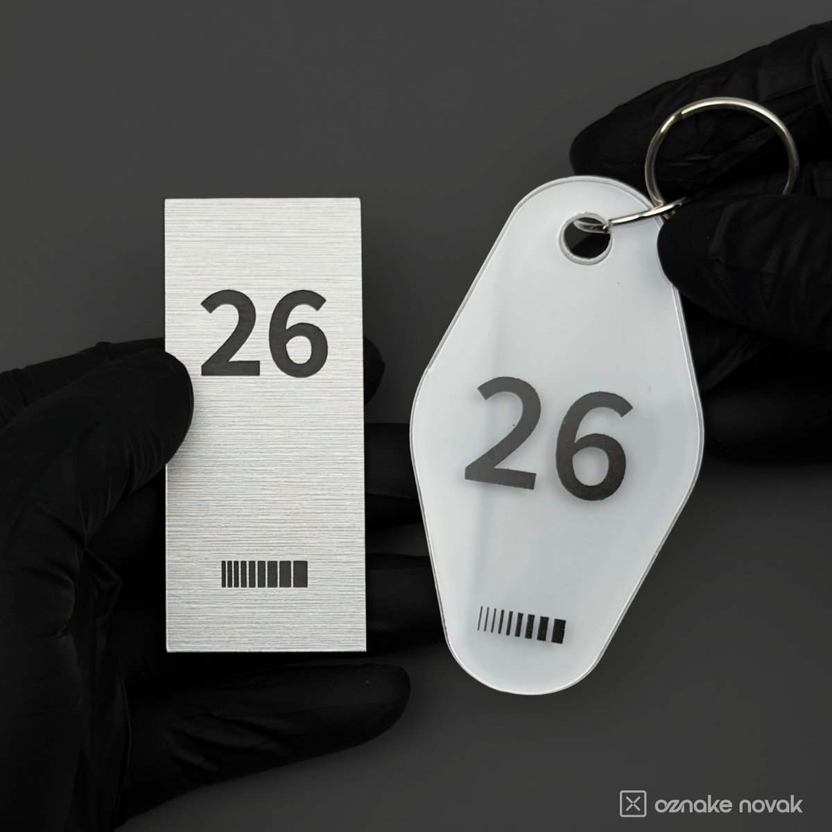 Gloved hands holding a brushed pewter plate and an opal white key tag, both numbered 26