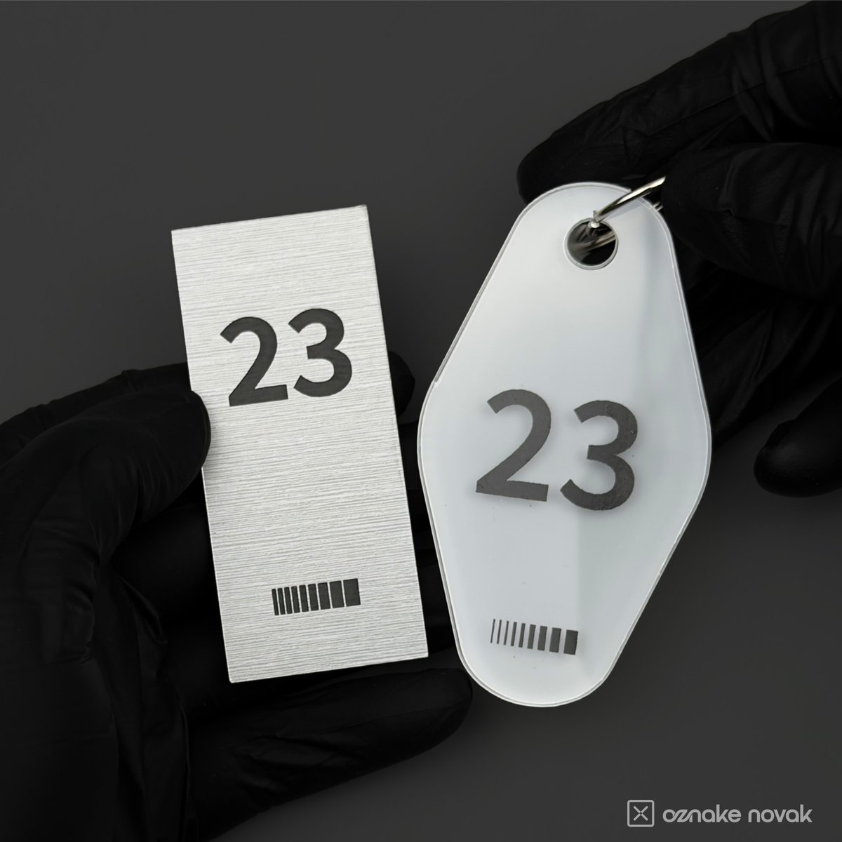 Gloved hands holding a brushed pewter plate and an opal white key tag, both numbered 23