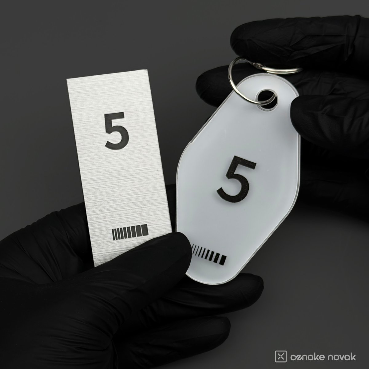 Gloved hands holding a brushed pewter plate and an opal white key tag, both numbered 5
