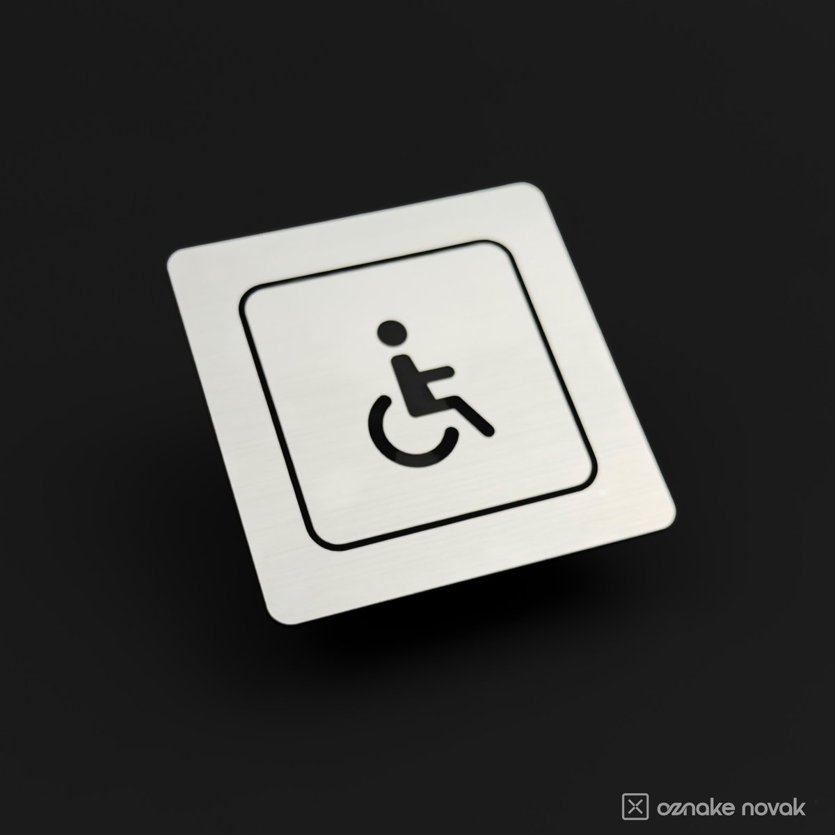 Brushed silver restroom sign with engraved accessible pictogram on a dark background