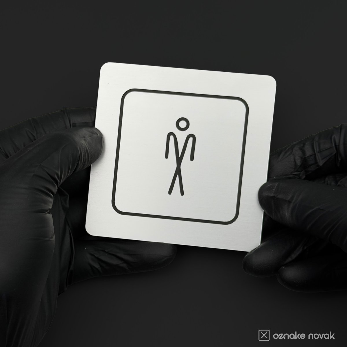 Gloved hands holding a brushed silver restroom sign with men's pictogram