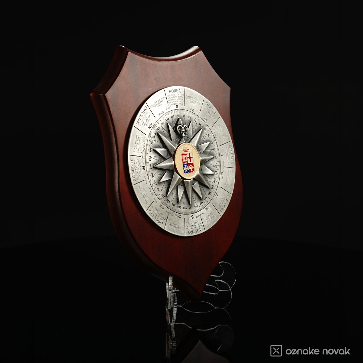 Wooden shield plaque with a silver compass rose emblem and enamelled coat of arms at the centre, on a clear stand