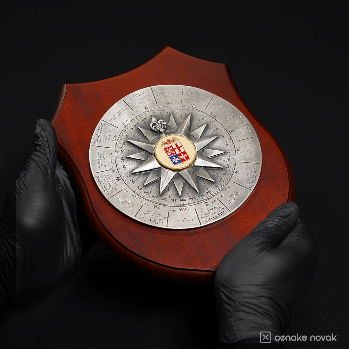 Gloved hands holding a wooden shield plaque with a silver compass rose emblem