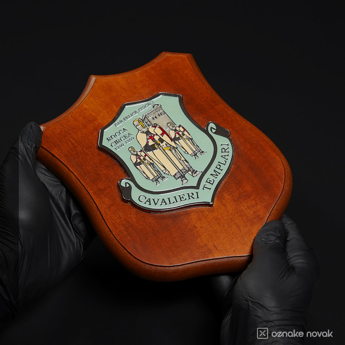 Gloved hands holding a wooden shield plaque with the Cavalieri Templari relief emblem