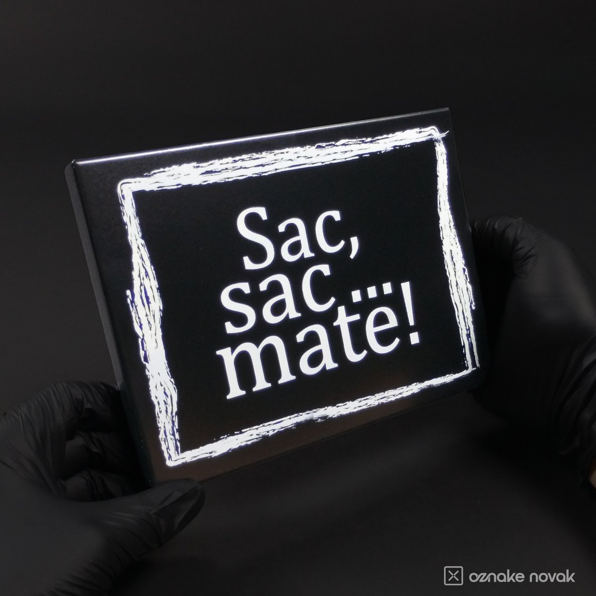 Gloved hands holding the black Sac, sac... mate! stainless steel name plate
