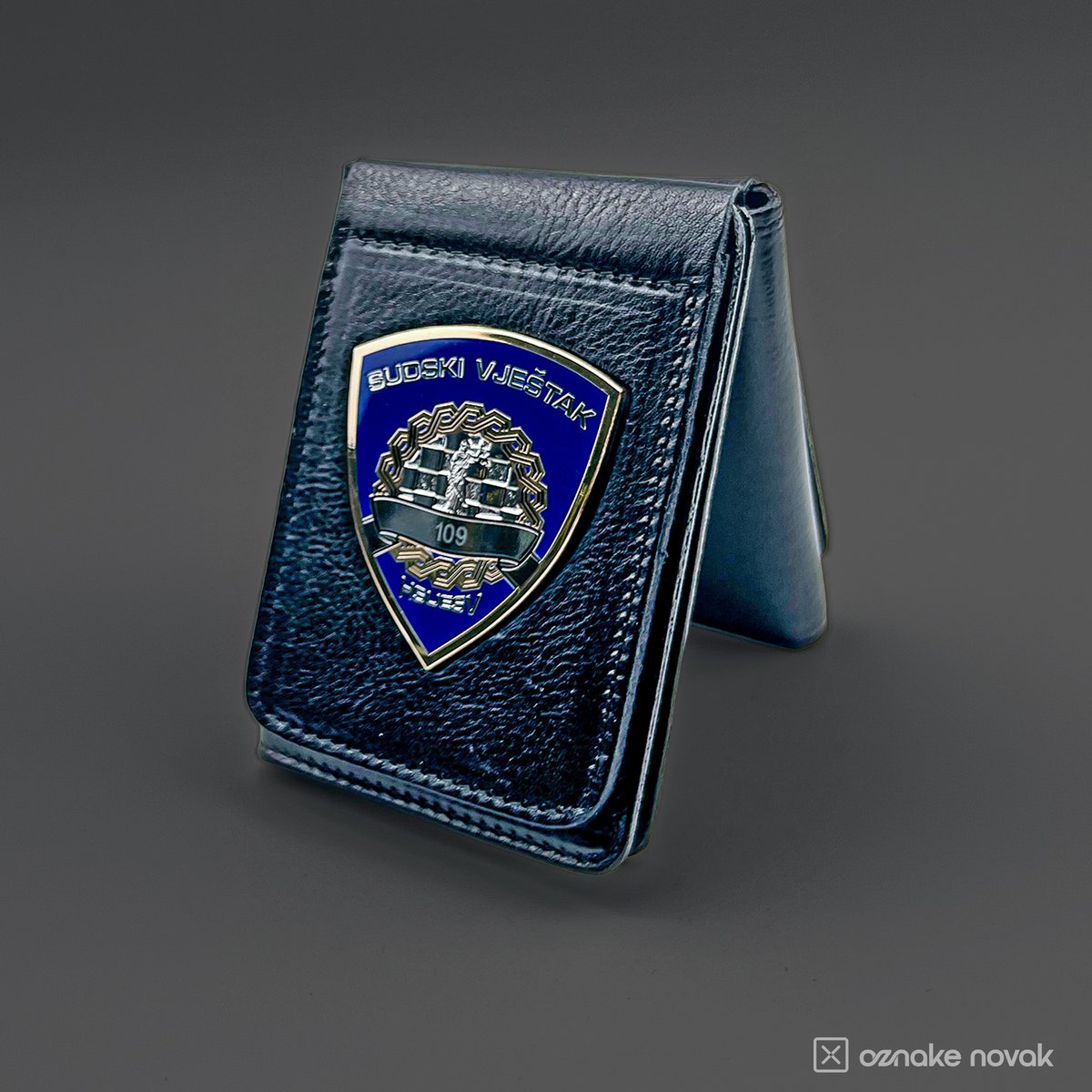 Opened black leather case standing upright with an enamelled court expert badge
