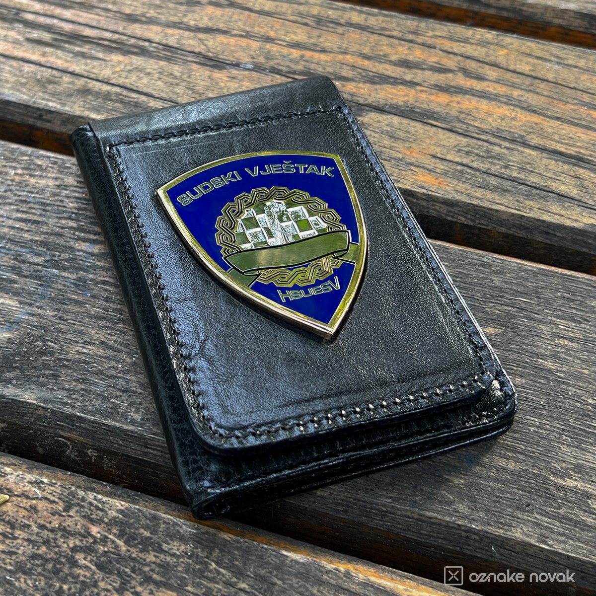 Black leather case with an enamelled court expert badge on a wooden bench