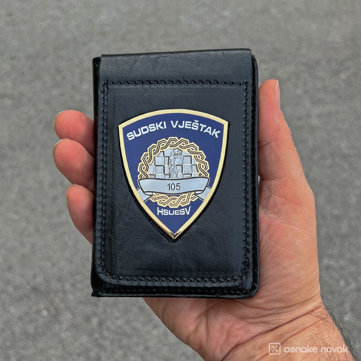 Hand holding a black leather case with HSUESV badge number 105